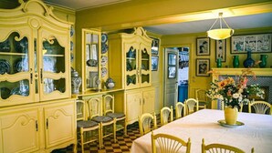 Une salle à manger avec un sol à carreaux, des chaises jaunes, une table recouverte d’une nappe blanche et un buffet jaune aux portes vitrées.