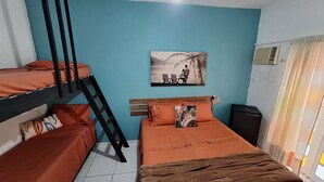 A dormitory room with bunk beds, a single bed, a ceiling fan, a wall-mounted air conditioner, and a window with curtains. - Pousada Oca Poranga (Guarujá)