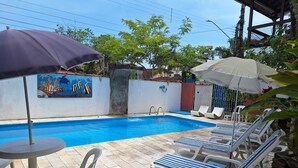A swimming pool with lounge chairs and umbrellas, surrounded by a tiled patio area. - Pousada Oca Poranga (Guarujá)