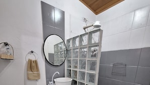 A bathroom with a toilet, sink, mirror, and shower. - Pousada Oca Poranga (Guarujá)