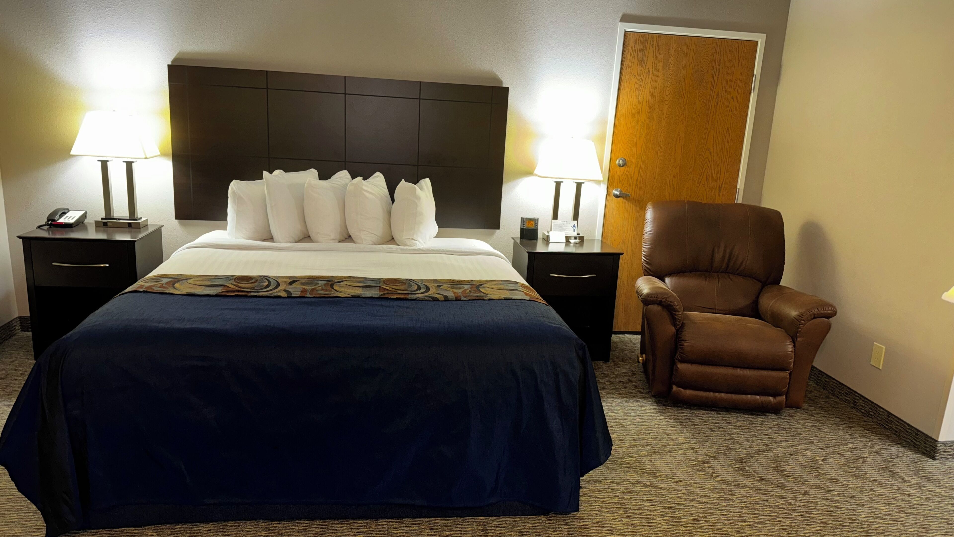 Una habitación de hotel con una cama, dos mesitas de noche, una silla y una puerta.