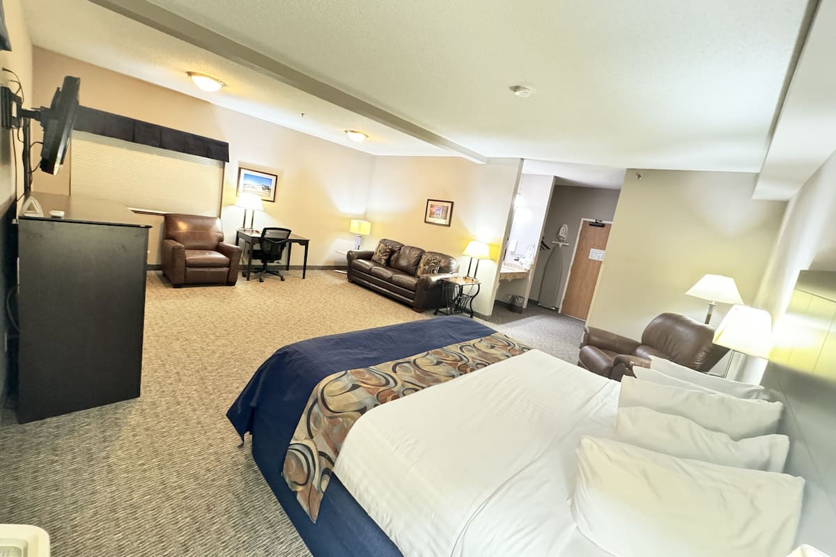 A hotel room with a bed, a desk, a chair, a sofa, and a refrigerator.