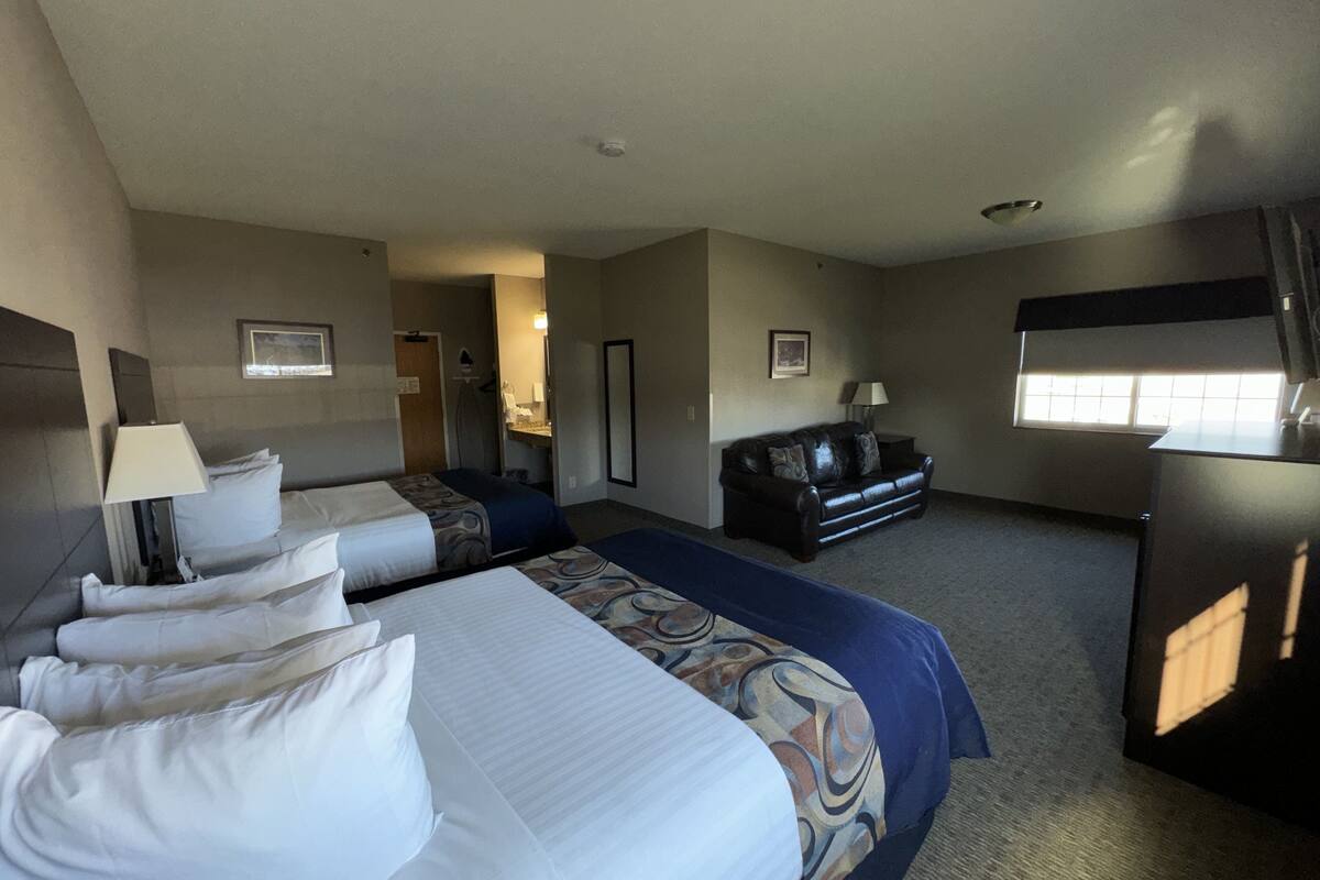 A hotel room with two beds, a sofa, a desk, and a window.