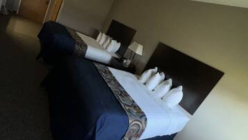 A hotel room with two beds, a carpeted floor, a door, and a nightstand with a lamp.