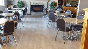 A spacious room with a fireplace, a television mounted above it, and a dining area with tables and chairs. - Garner Inn & Suites (Garner)