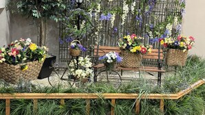 A garden area with wicker baskets filled with flowers, a wooden bench, and a metal fence with climbing plants. - Garner Inn & Suites (Garner)