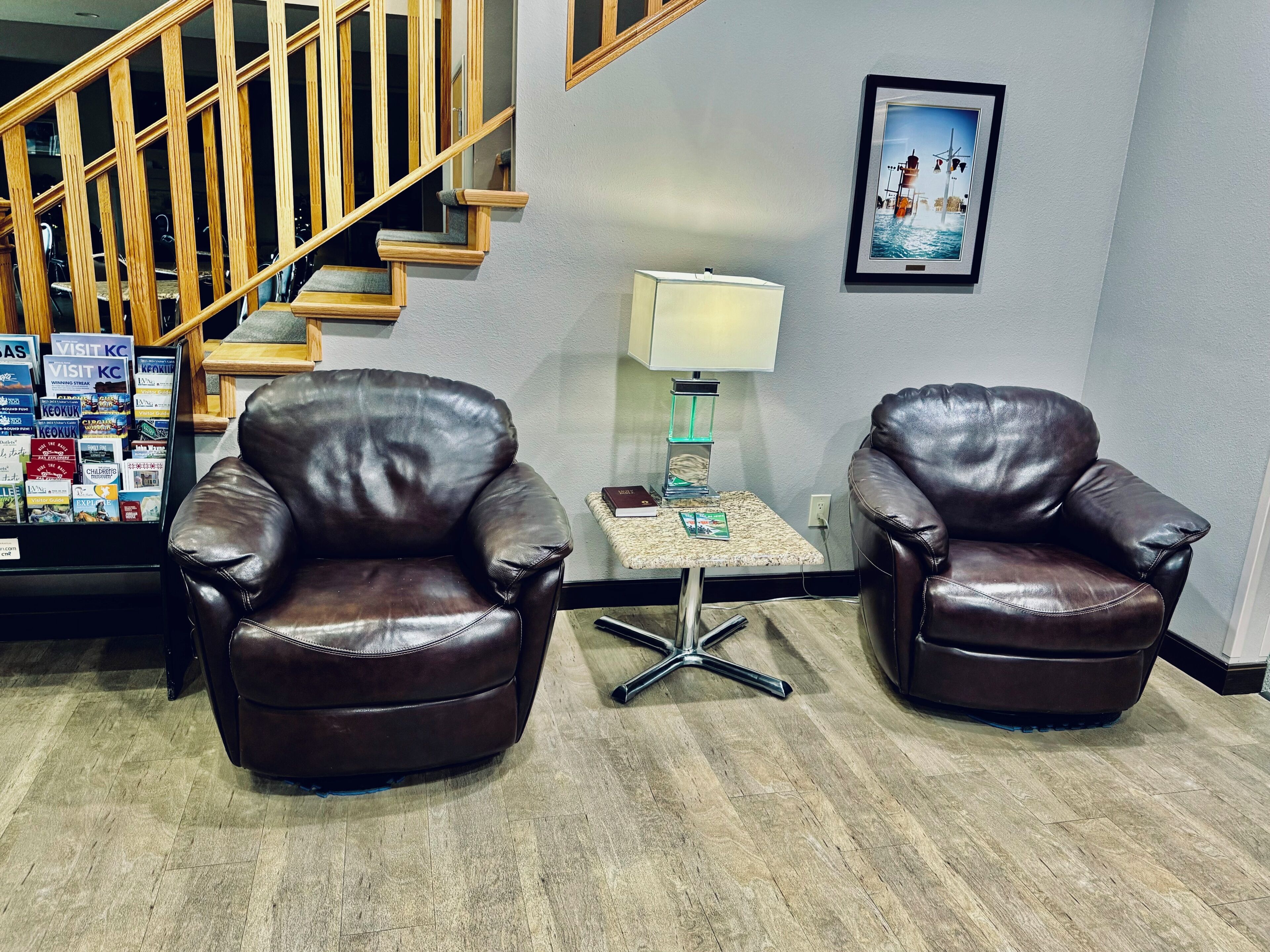 Una habitación con dos sillones de cuero, una mesita con una lámpara, un cuadro en la pared y una escalera.