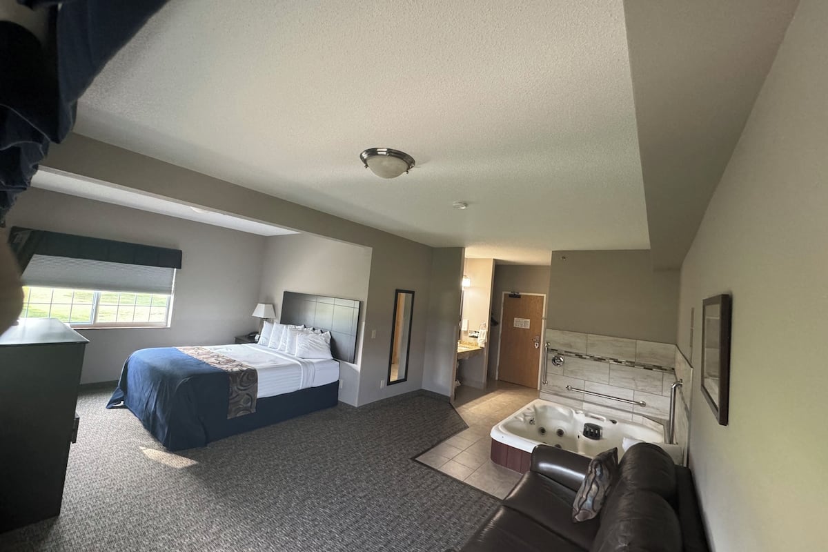 A hotel room with a bed, a desk, a sofa, a hot tub, and a bathroom.