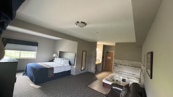 Hotellihuone, jossa on sänky, työpöytä, sohva, kylpyammeella varustettu kylpyhuone ja ikkunassa sälekaihtimet.