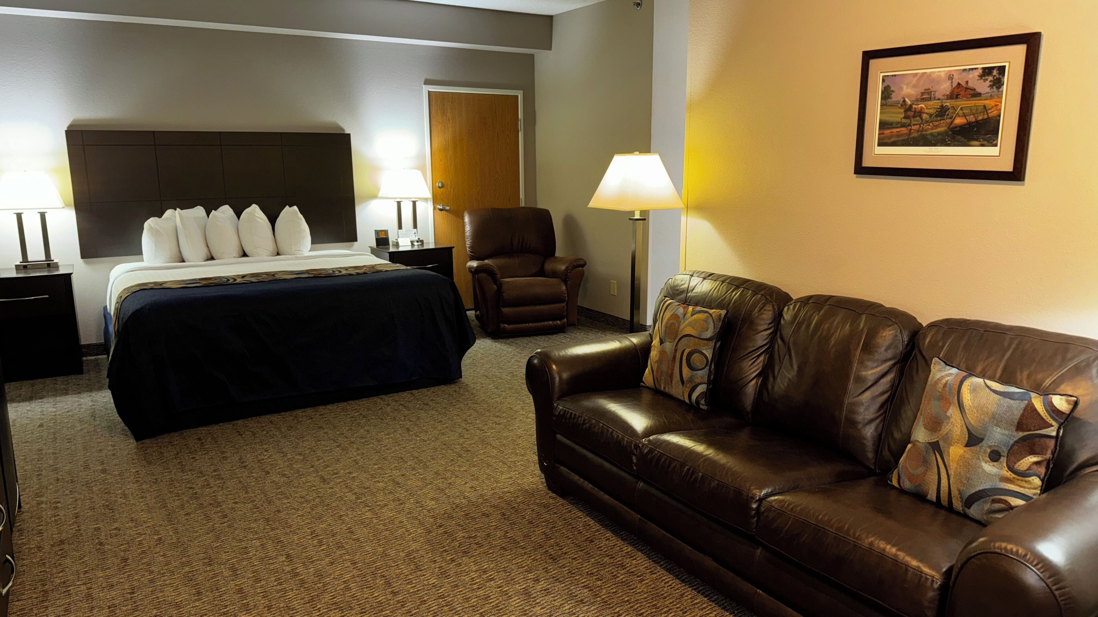 A hotel room with a bed, a leather sofa, a chair, and a lamp.