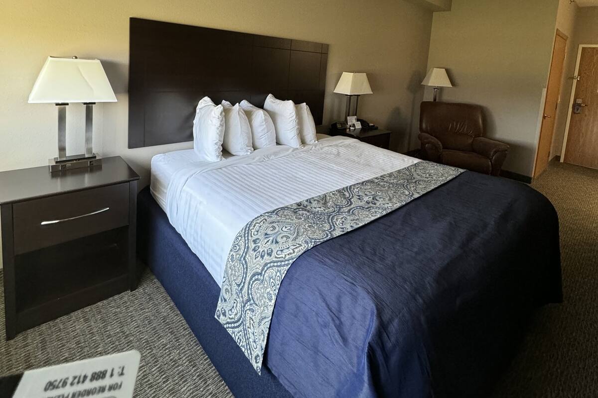 A hotel room with a large bed, two bedside tables with lamps, a chair, and a door.