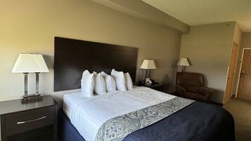A hotel room with a large bed, two bedside tables with lamps, a chair, and a door.