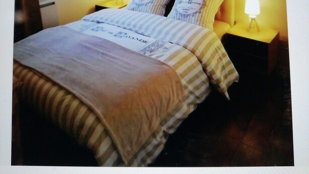 Un dormitorio con cama, dos mesitas de noche, un estante en la pared con objetos decorativos y una ventana.