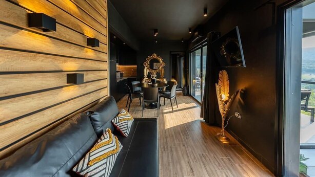 Un intérieur moderne avec un canapé en cuir noir, un mur lambrissé en bois et un coin repas comprenant une table ronde et des chaises.