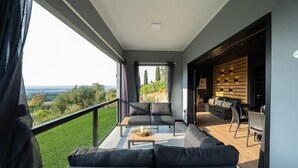 Un salon moderne doté d’un grand balcon, d’un canapé, d’une table basse et d’un coin repas avec un mur en bois et une vue sur la campagne.