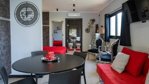 A modern living room with a red sofa, a dining table with chairs, a globe wall clock, and a TV mounted on the wall. - One-room Apartment "Suite Love" with View (SCARLINO)