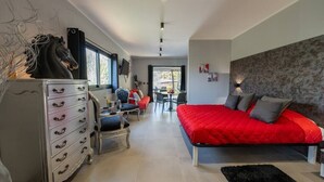 A modern bedroom with a red bedspread, a dresser with multiple drawers, a chair, a desk, and a television mounted on the wall. - One-room Apartment "Suite Love" with View (SCARLINO)