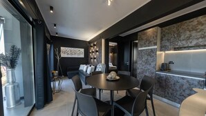 A modern dining area with a round table and chairs, a sofa, and a kitchen area with a marble backsplash. - Passion Suite with Garden and Whirlpool (SCARLINO)