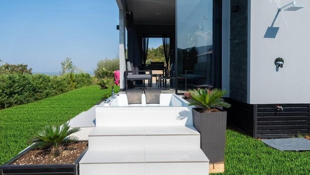 A modern house with a glass door leading to an outdoor seating area. - Passion Suite with Garden and Whirlpool (SCARLINO)