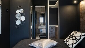 A modern bedroom with a dark color scheme, a bed with patterned pillows, and a wall art piece. - Passion Suite with Garden and Whirlpool (SCARLINO)