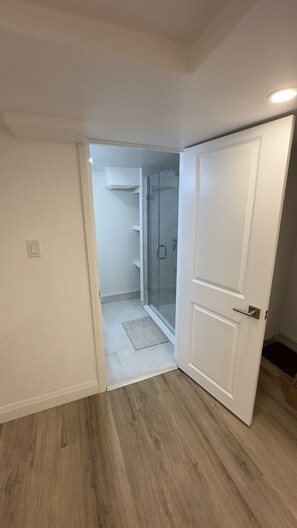 Une pièce avec un plancher en bois, une porte blanche et une cabine de douche en verre.