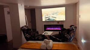 A hotel room with a bed, a TV mounted on the wall, a fireplace, and a view of a cityscape.