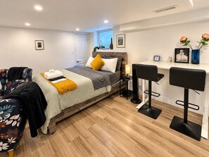 A modern hotel room with a bed, a desk with two chairs, a window with a view, and a wooden floor.