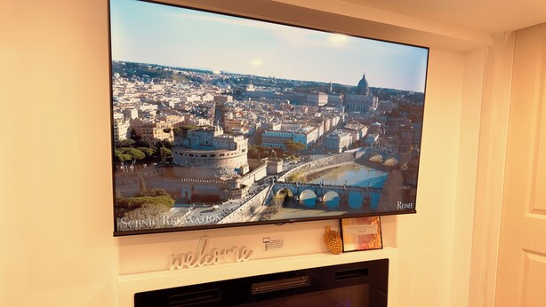 A flat-screen TV mounted on a wall displaying a scenic cityscape with a prominent dome structure. Below the TV, there is a fireplace with a visible fire.