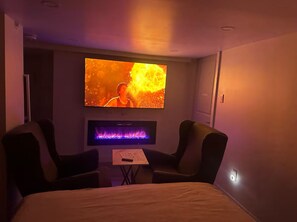 Une chambre d’hôtel avec un grand lit, deux fauteuils, un téléviseur à écran plat et une petite table avec une télécommande.