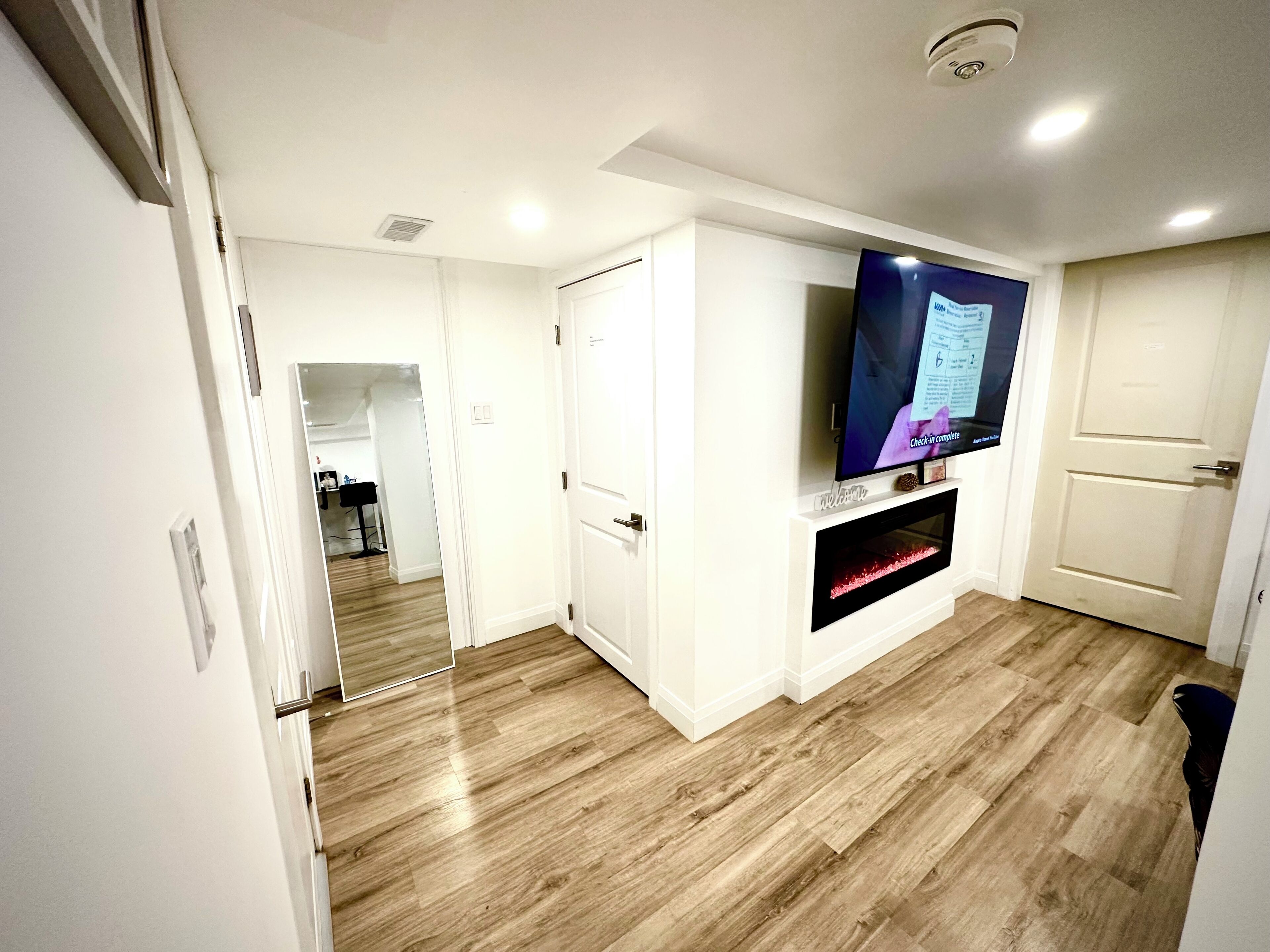 A modern living room with a flat-screen TV mounted on the wall, a fireplace, and wooden flooring.