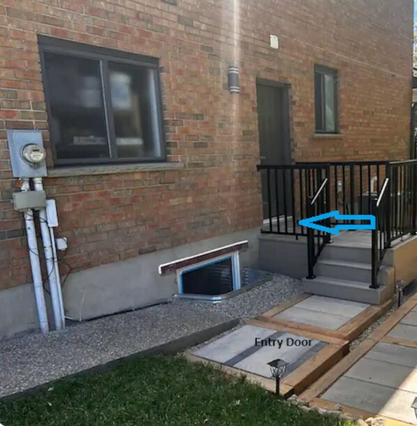A brick building with a metal railing, an entry door, and a window.