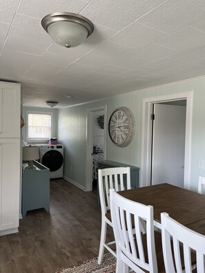 A compact kitchen with a dining area, a washing machine, and a large wall clock. - Lakeview Cottage, Walk to the beach, parks & downtown. Early booking discount! (Ludington)