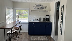 Una cuina amb taula de fusta, tamborets, una cafetera i un rètol que diu "BEACH HOUSE".