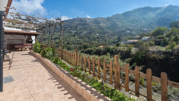 A patio with a wooden fence, a table, and chairs, overlooking a mountainous landscape with houses. - Casa Abuela - House in the countryside with pool (Vega de San Mateo)