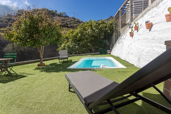 A backyard with artificial grass, a swimming pool, a lounge chair, and potted plants.