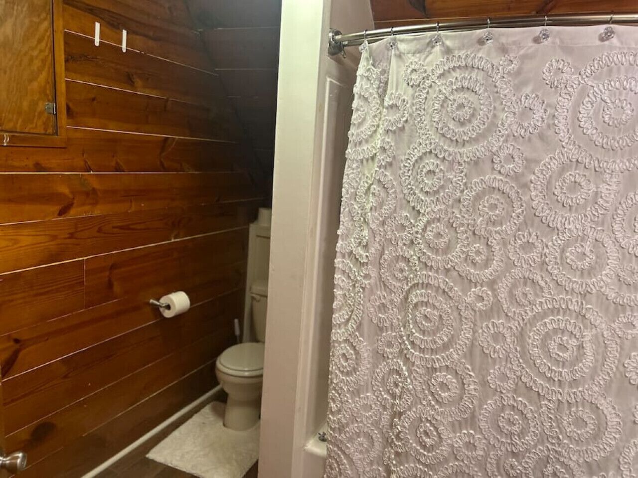 Un bagno con pareti in legno, un WC e una tenda da doccia con motivo floreale.