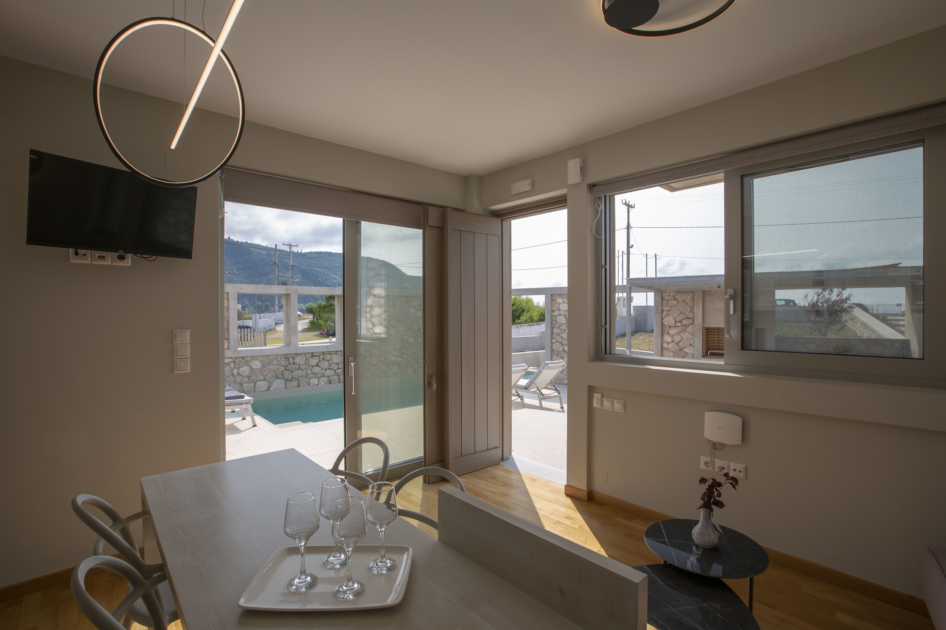 A modern dining area with a table set for two, a view of a pool, and a balcony with outdoor furniture.