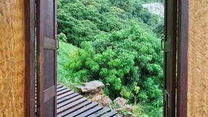 A wooden door leading to a lush green garden with a thatched roof overhead. - MonLomNao Homestay (Mae Rim)