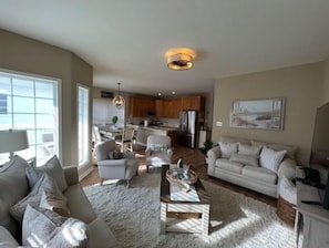 A spacious living room with a large window, a kitchen in the background, and a dining area. - Ocean Sunrise Unit 100 Completely Refreshed for Summer 2026 (Wildwood)