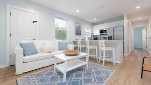Et moderne køkken med hvide skabe, en central ø og et spiseområde med hvide stole og et bord.