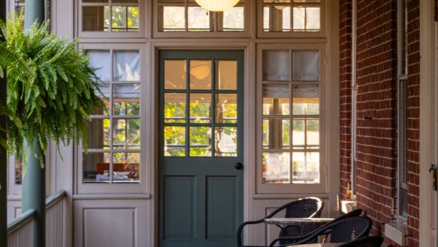 A covered porch with a green door, wicker furniture, and a hanging light fixture. - The Lafayette Inn (Easton)