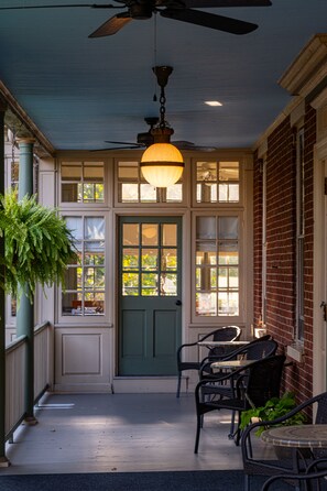 A covered porch with a green door, wicker furniture, and a hanging light fixture. - The Lafayette Inn (Easton)