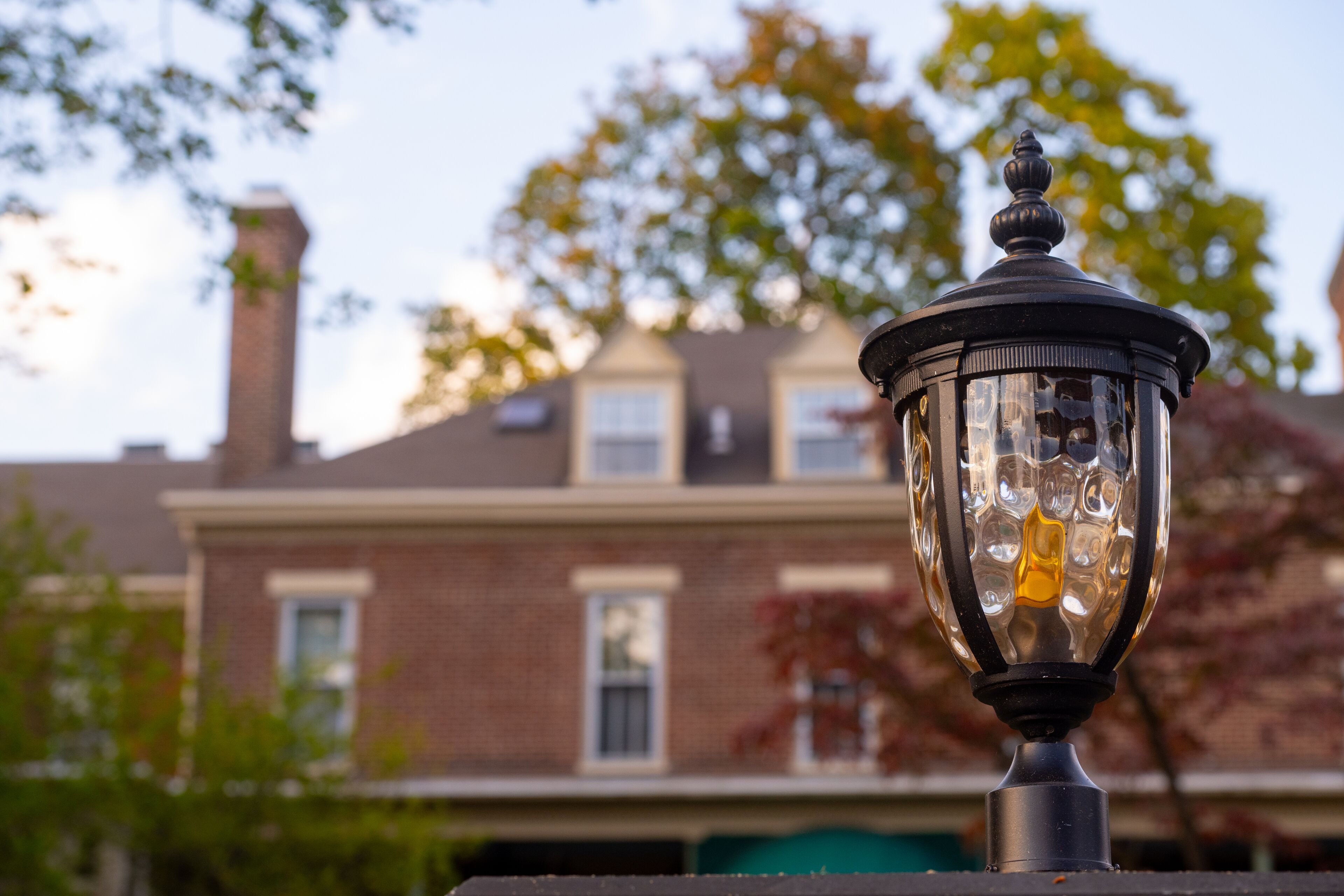 A street lamp with a clear view of a brick building with a chimney in the background.
