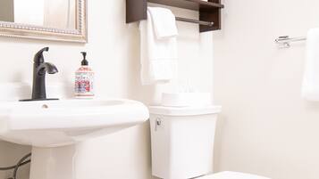 A bathroom with a white sink, black faucet, white toilet, and a black trash bin.