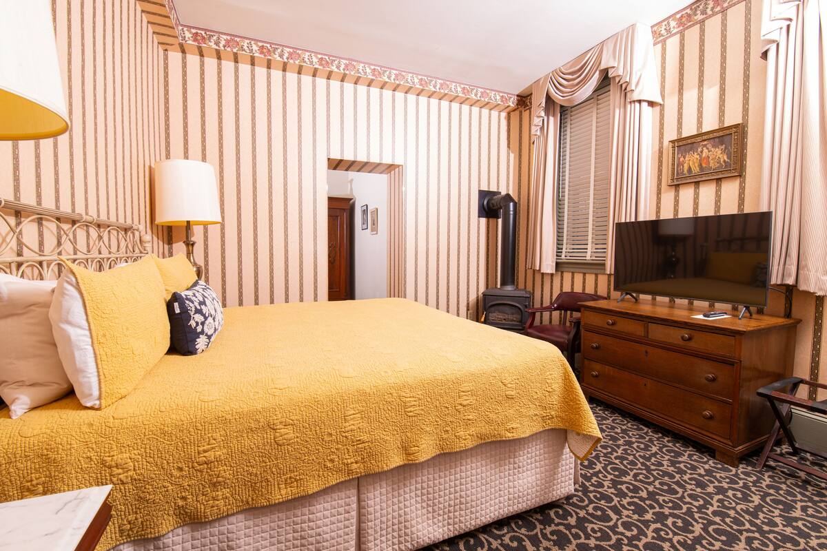 A hotel room with a large bed, a dresser, a television, and a door leading to another room.