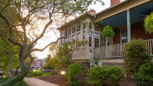 A two-story house with a front porch, a brick facade, and a small garden area with shrubs and a tree. - The Lafayette Inn (Easton)