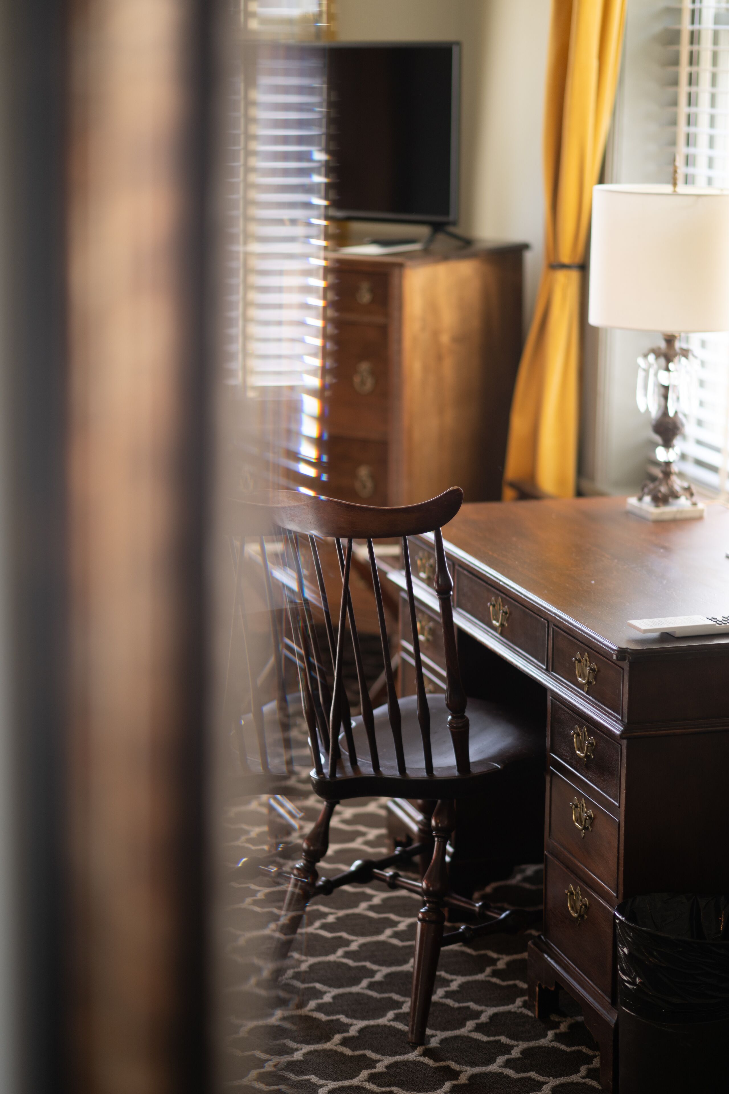 Un bureau en bois avec des tiroirs, une chaise et une lampe.