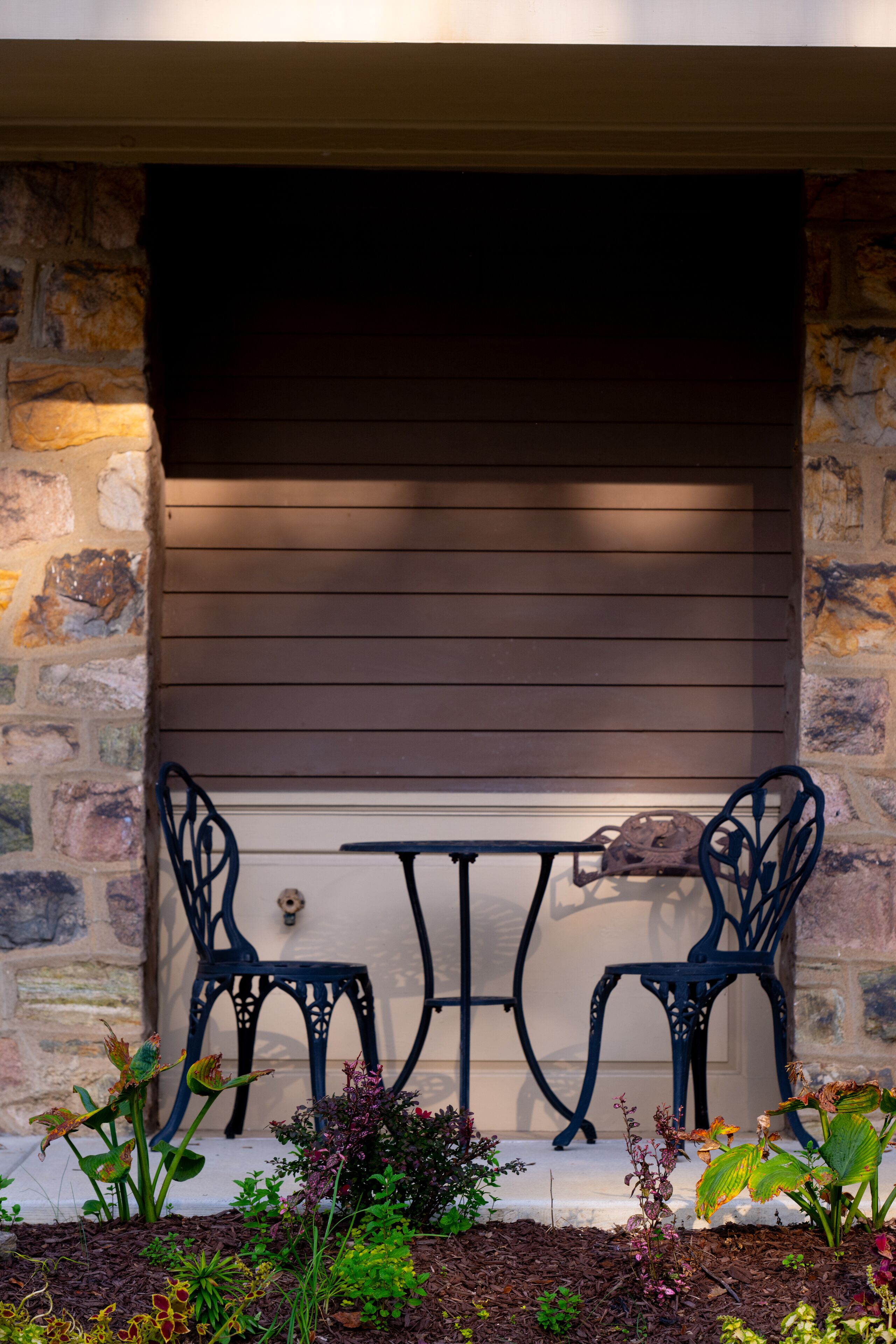 A patio with two metal chairs and a table, set against a stone wall with wooden siding above.