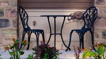 A patio with two metal chairs and a table, set against a stone wall with wooden siding above.