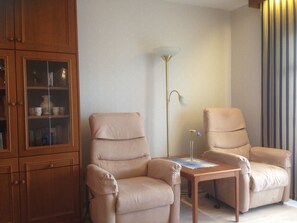 Un salon avec deux fauteuils beiges, un meuble en bois doté de portes en verre et un lampadaire.